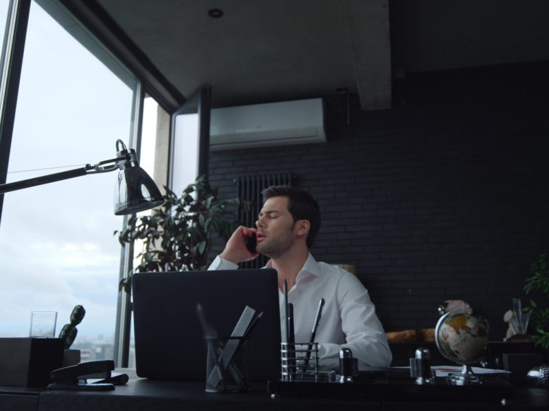 Handsome businessman answering on phone call at remote workplace. Serious manager talking on smartphone in office interior. Portrait of confident business man working in modern office