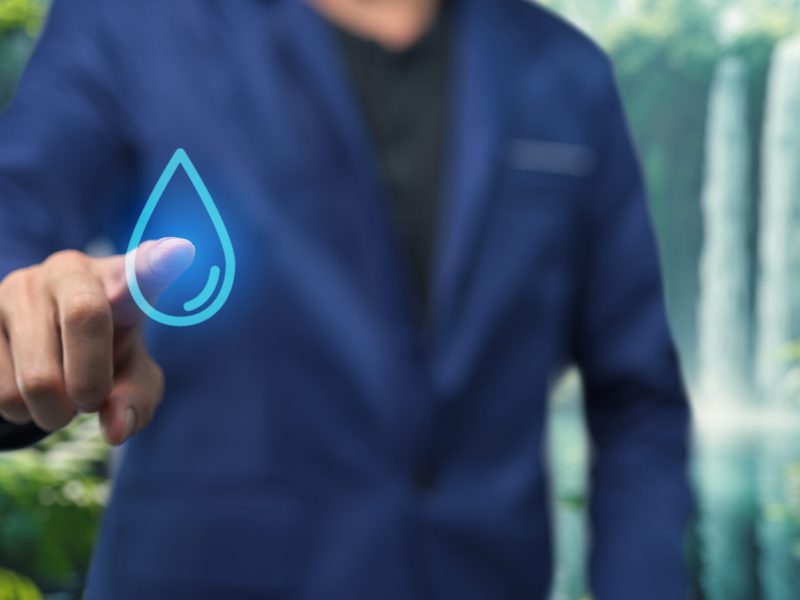 A person interacts with a digital water drop symbol, promoting water conservation awareness in a lush, natural setting. Emphasizes the importance of resource management.